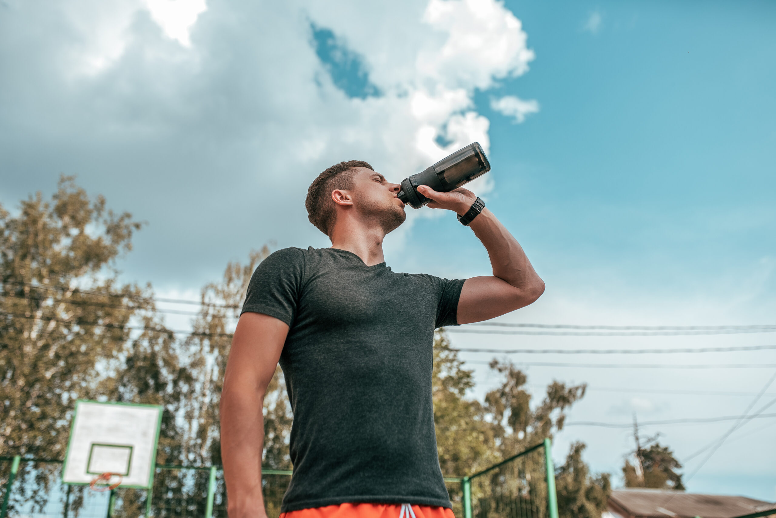 Male athlete, drinking water and protein from shaker, fitness watch, training in the city in the fresh air. Concept morning run in the city, fitness and workout, smart watch bracelet. Sportswear T-shirt.